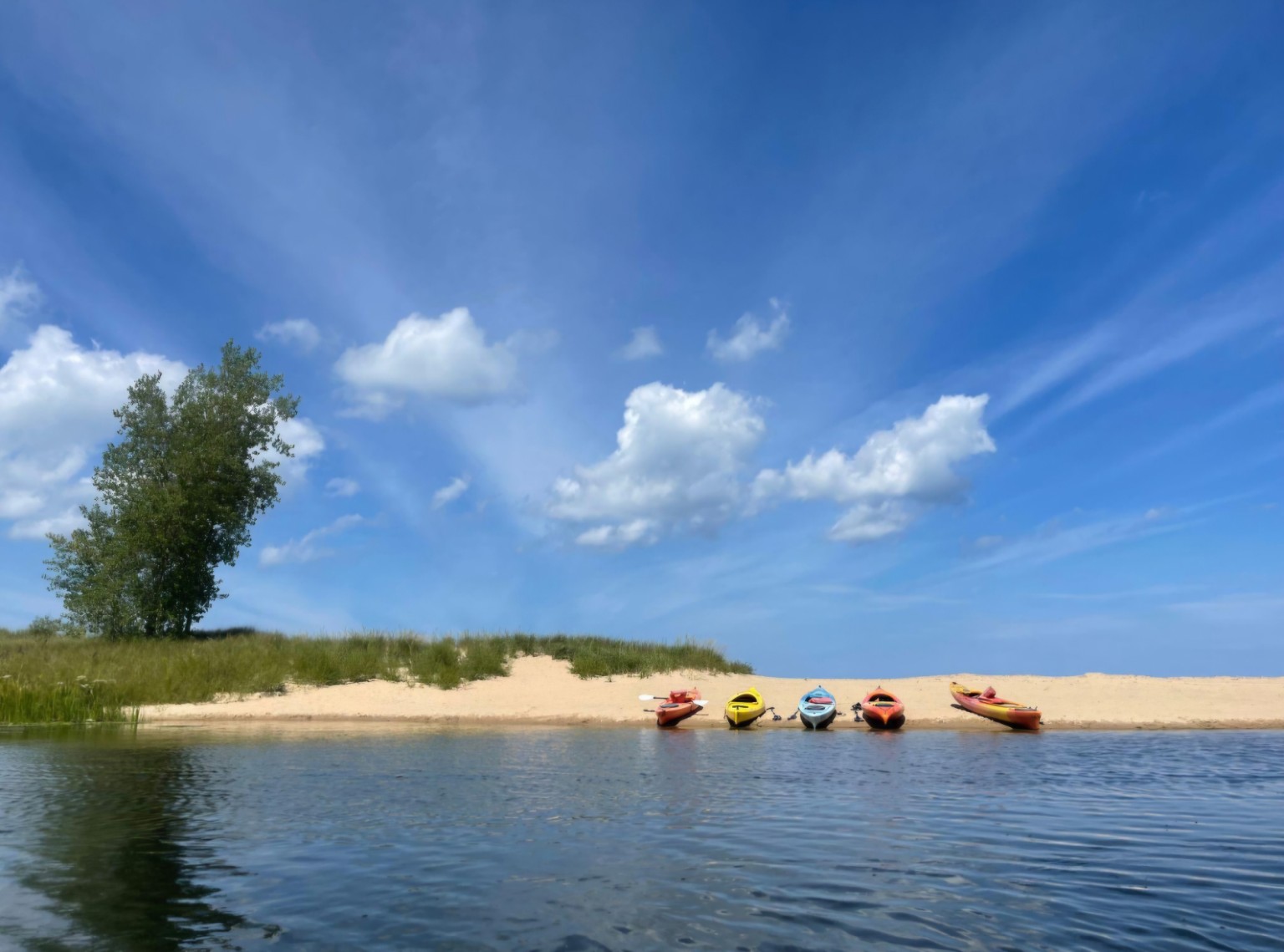Colorful kayaks resting on the sandy Port Crescent beach beside the Pinnebog River beneath a blue sky